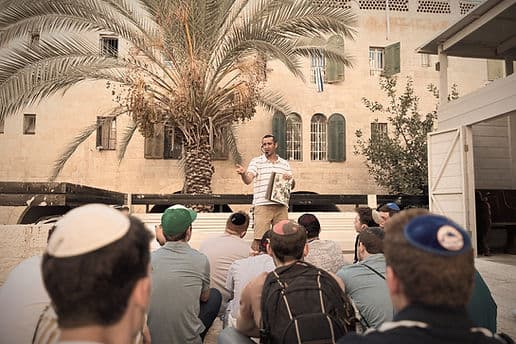 A guide speaking to a seated group of Torah Tech students in a Jerusalem courtyard